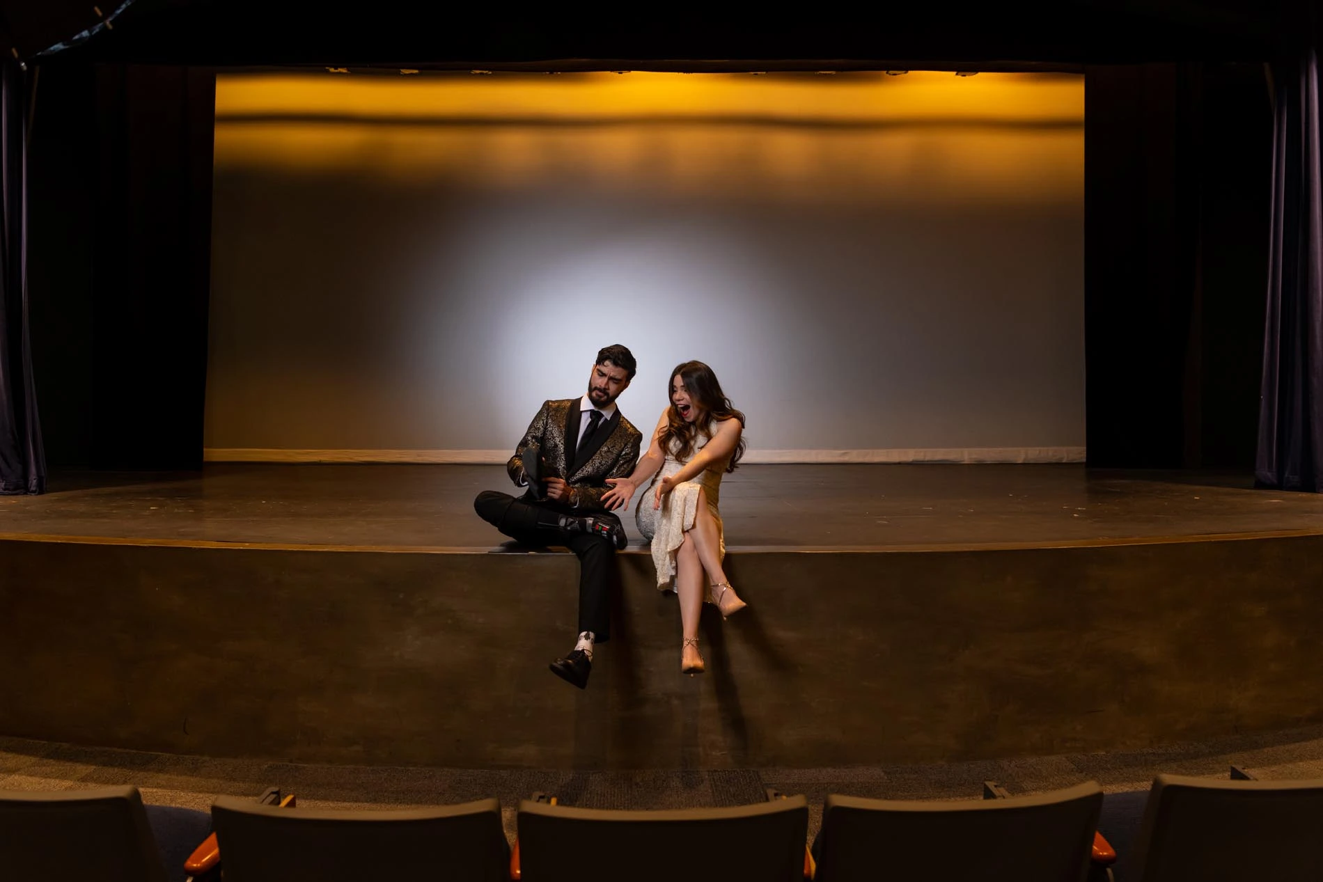 Couple sitting on a stage of an empty theater, girl is admiring the boyfriend's Star Wars socks