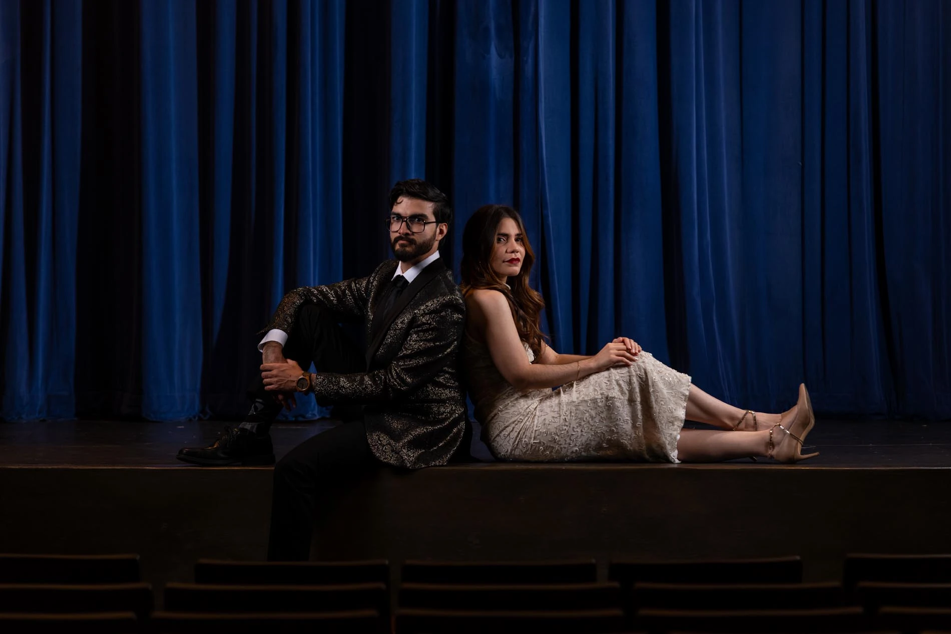 Couple sitting back to back in front of theater stage blue curtains