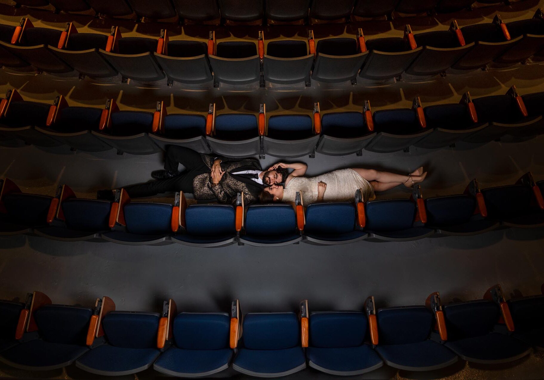 Couple laying down face to face on the floor between theater seats