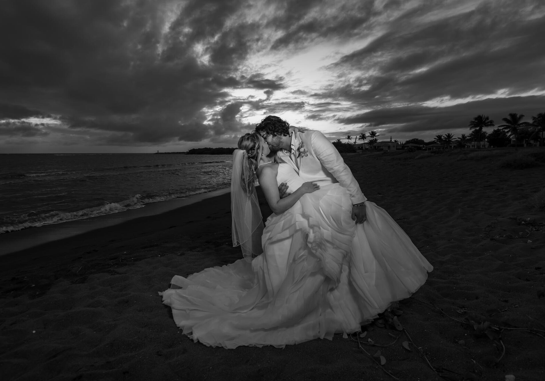 Black and white photograph of the newlyweds kissing in a deep pose on the beach
